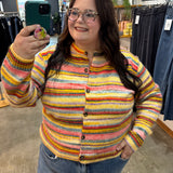 A woman taking a mirror selfie in a clothing store, wearing a colorful striped knit cardigan sweater with blue jeans.