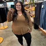 A woman takes a mirror selfie in a clothing store, wearing a tan long-sleeve knit sweater, black leggings, and brown sandals.